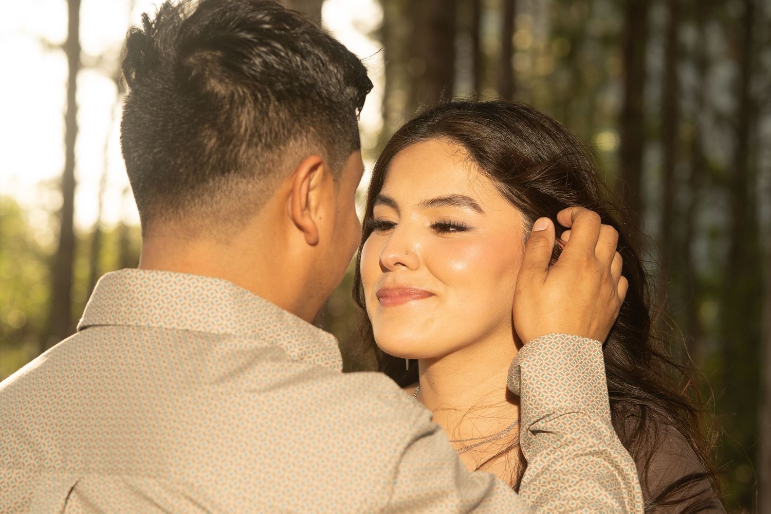 Romantic couple sharing a tender moment outdoors, man gently touching womans hair in golden sunlight.