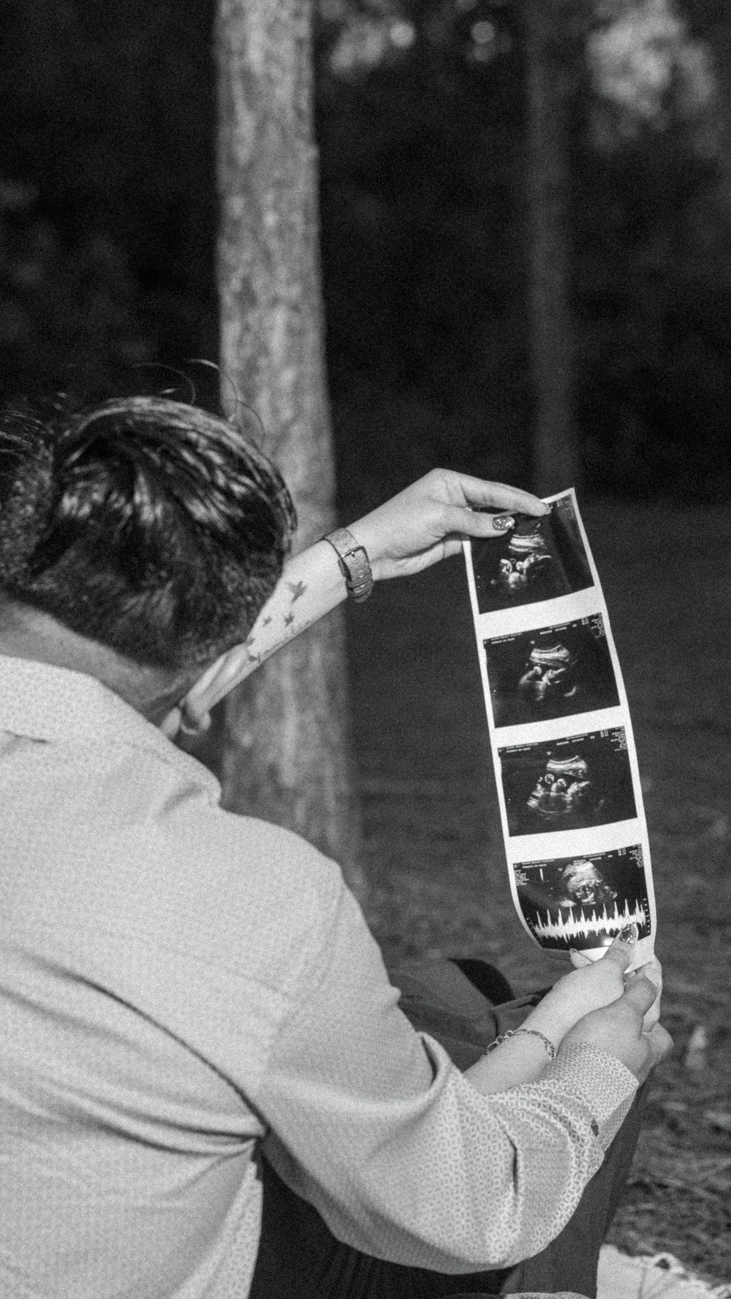 Couple holding ultrasound sonogram photos outdoors in black and white pregnancy announcement photo.