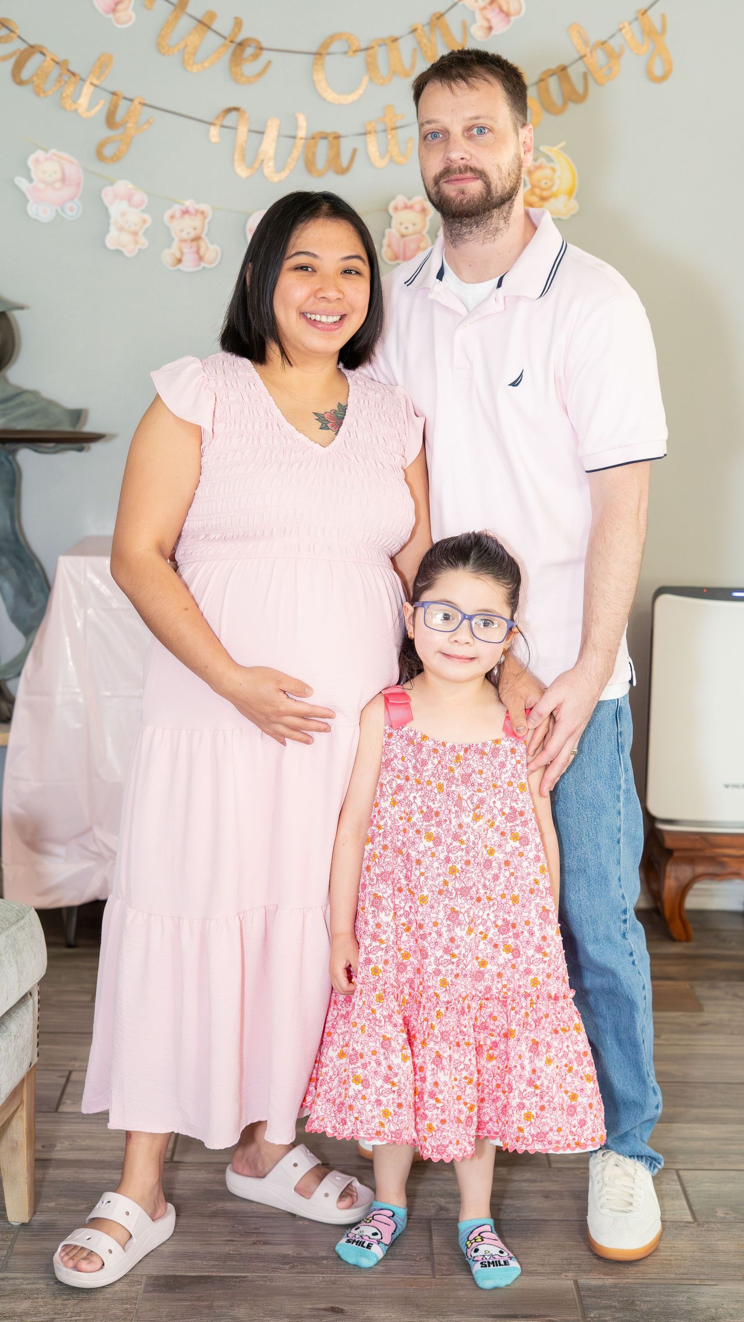 Pregnant woman in pink dress with husband and young daughter at a baby shower celebration.
