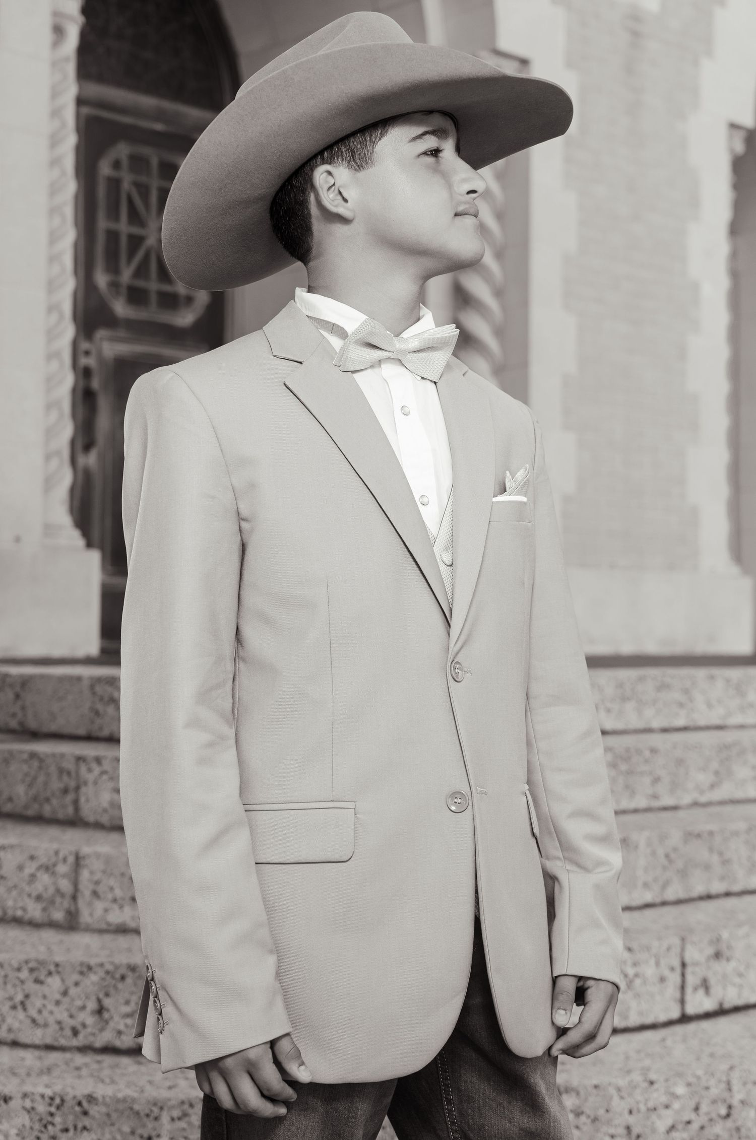 A vintage black and white photograph shows a young child in a light-colored suit jacket standing outdoors.