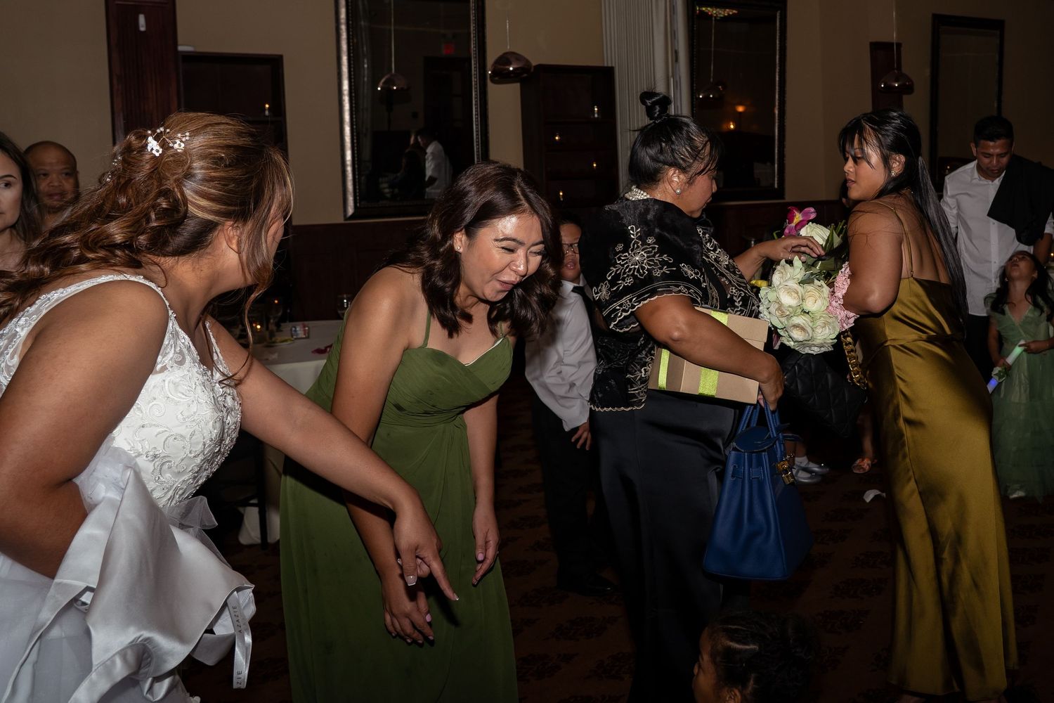 Wedding guests gather on the dance floor as a woman catches the bridal bouquet at a reception.