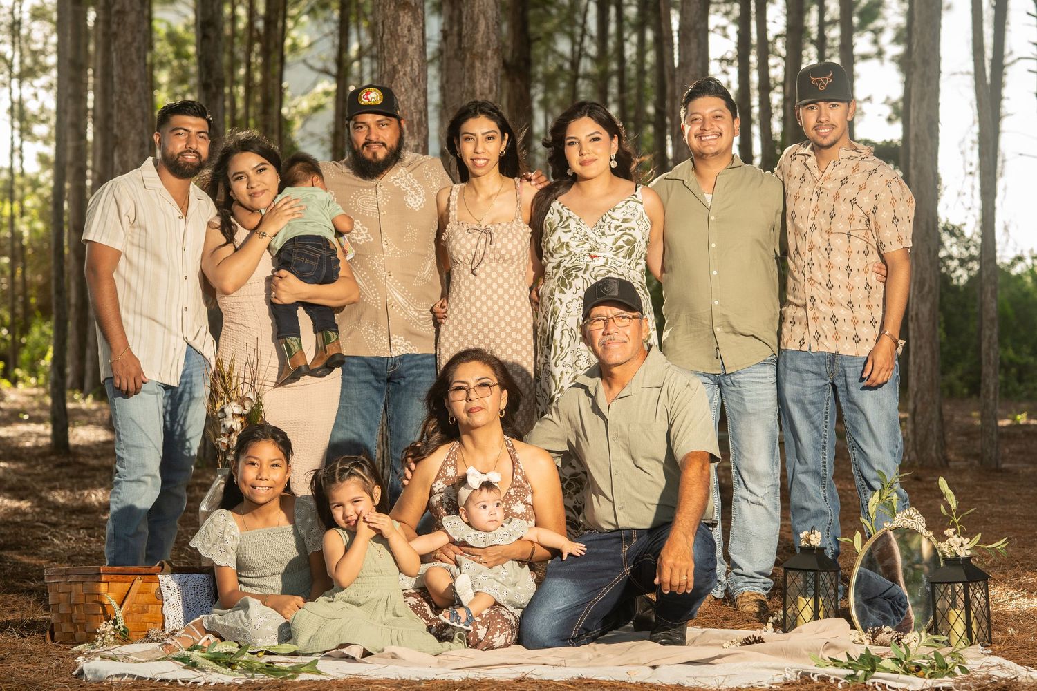 Large Hispanic family posing together outdoors in a pine forest for a professional portrait session.