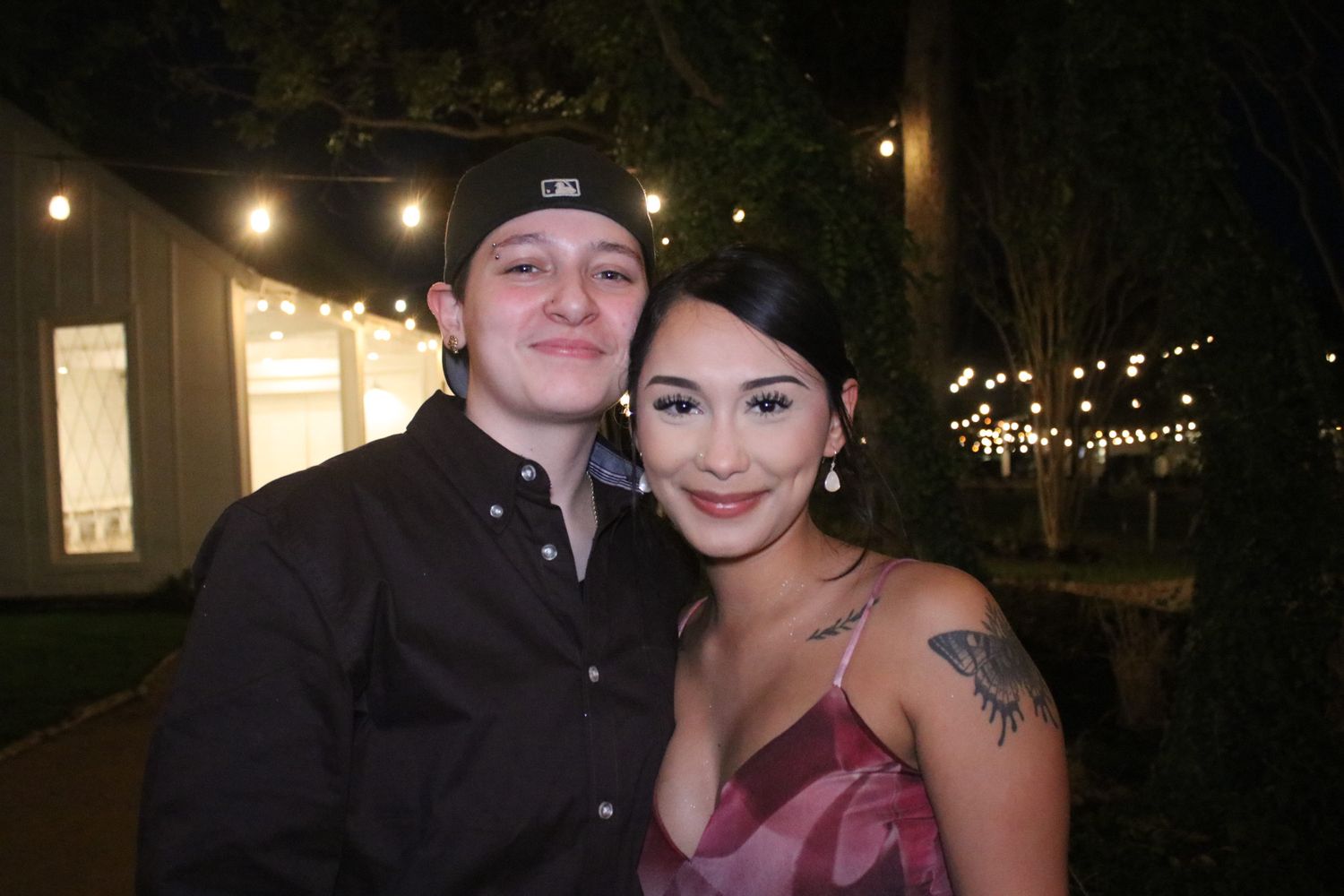 A couple poses together at night under string lights in a romantic outdoor setting.