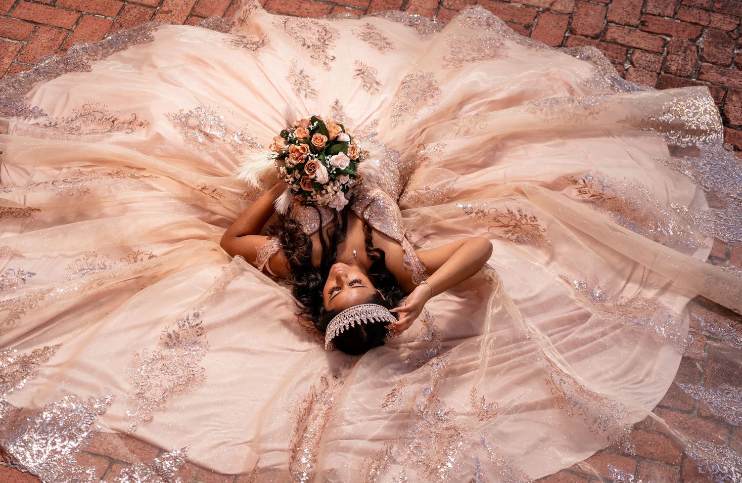 Aerial view of a luxurious champagne ballgown with intricate beadwork spread across brick pavement.