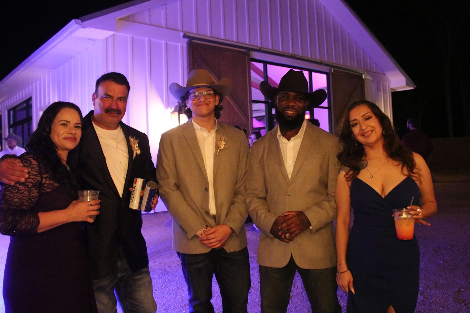 Group of five people posing together outside a purple-lit building at night.