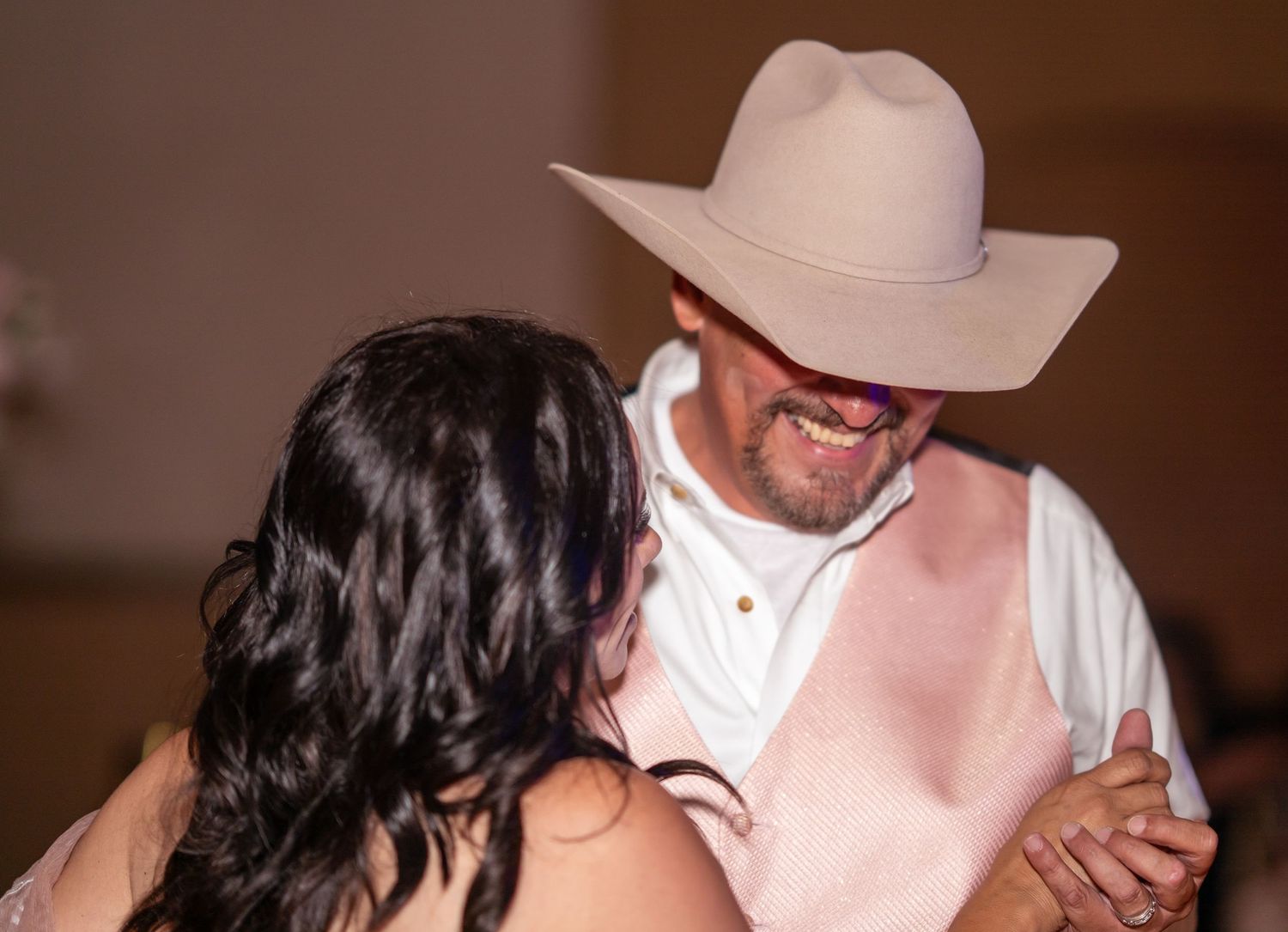 A smiling man in a cowboy hat shares a close dance with a dark-haired woman at a festive celebration.