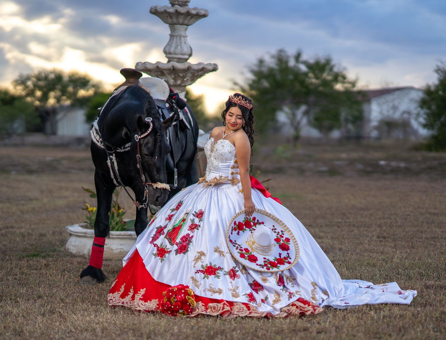 Sunset photoshoot featuring an ornate white and red ball gown next to a decorative fountain.
