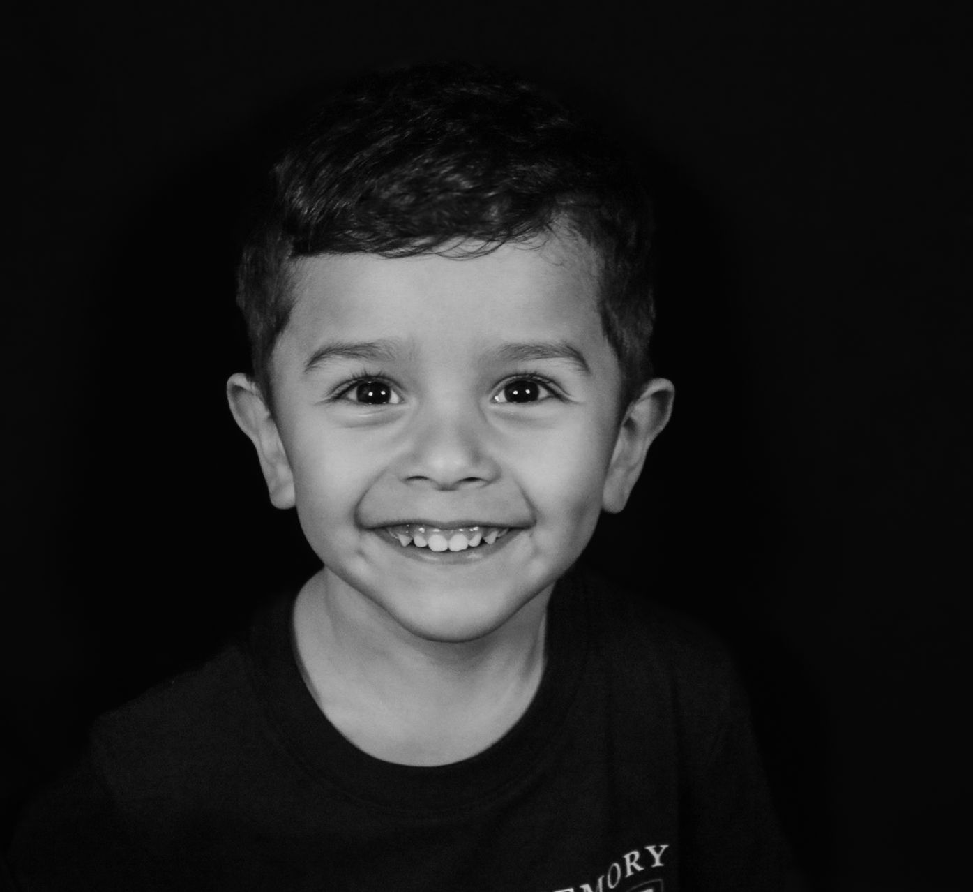 A black and white portrait of a young child smiling brightly.