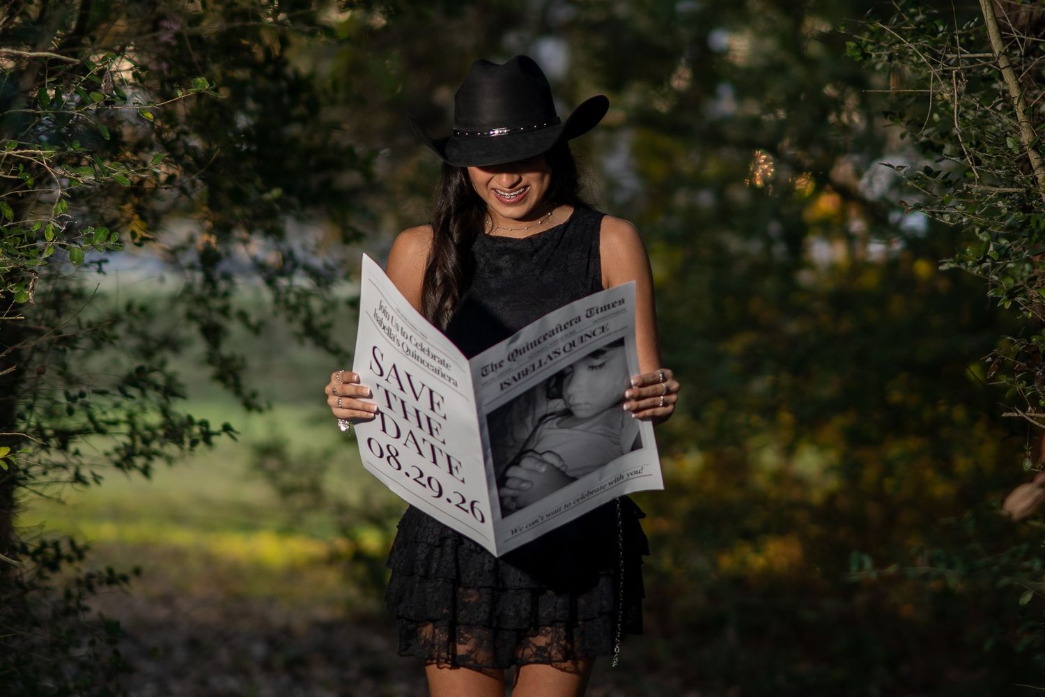 Woman in black dress and cowboy hat reads a save the date newspaper announcement outdoors.