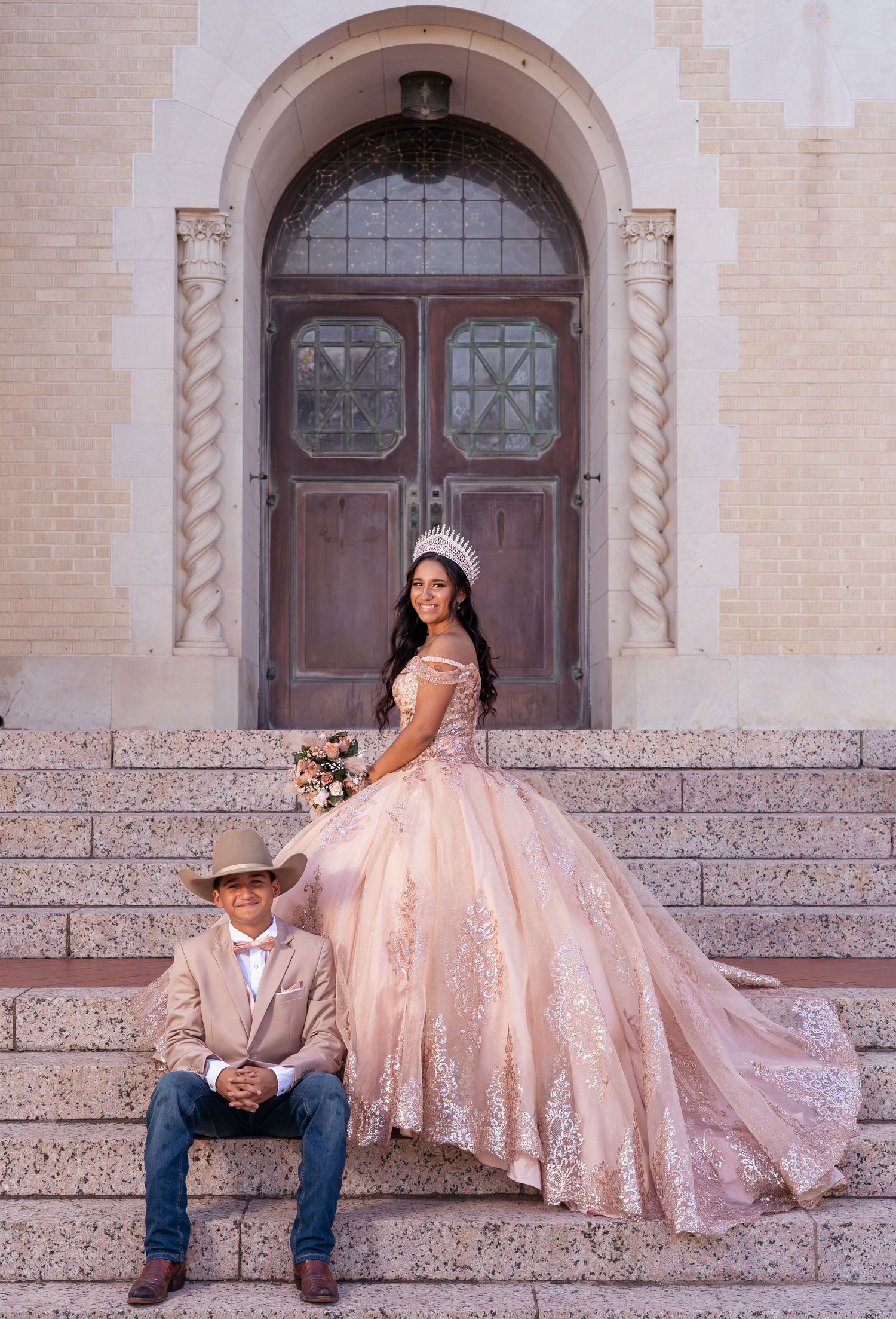 Couple in formal wear pose dramatically on stone steps of historic building with elegant architecture.