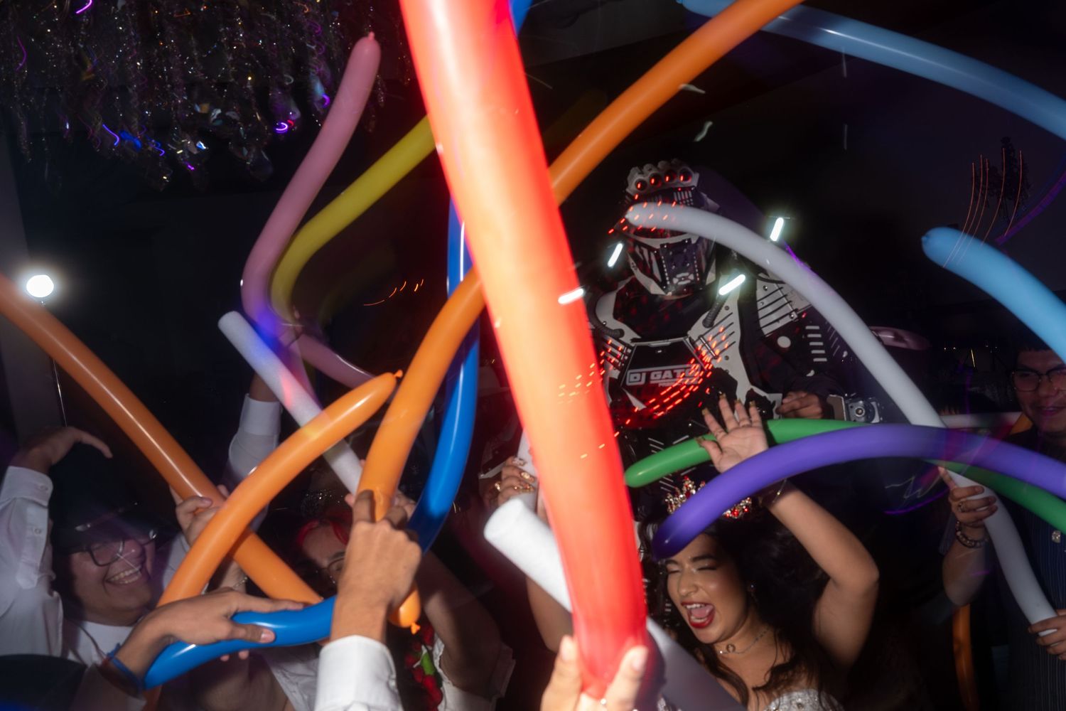 Colorful foam noodles wave through a dark nightclub atmosphere as party-goers dance beneath glowing lights.