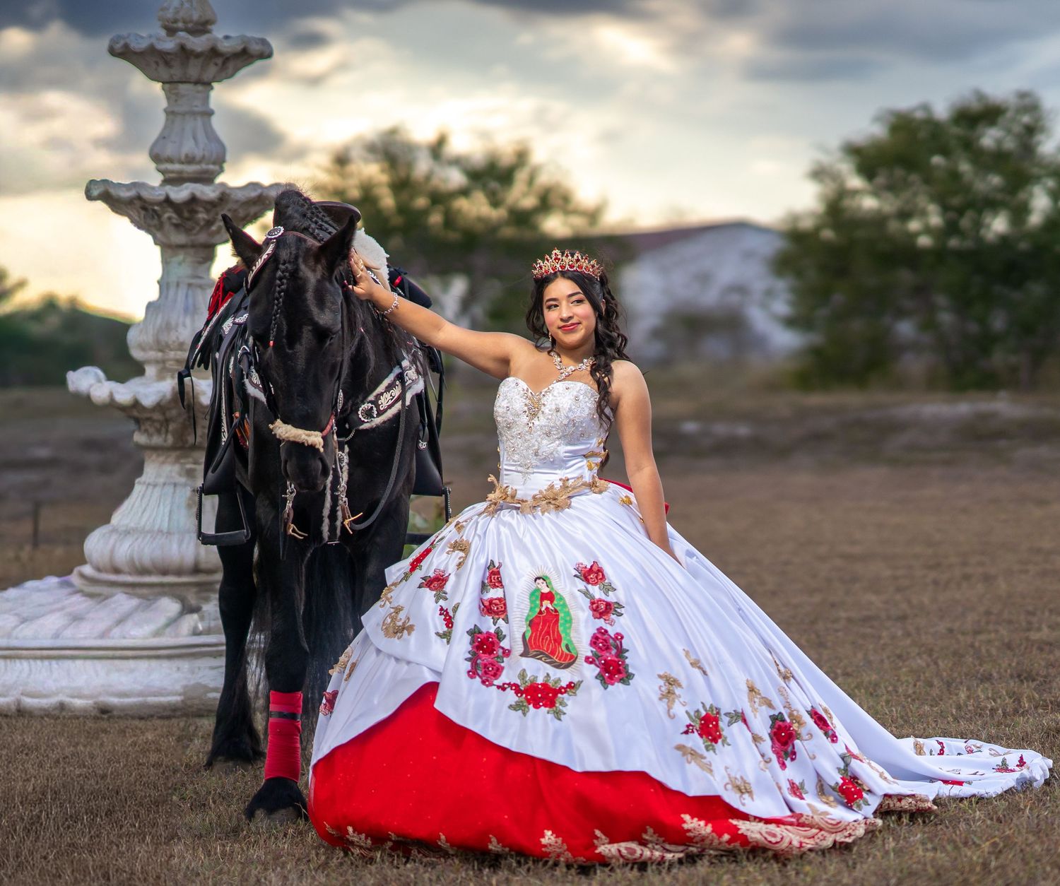An elegant white and red dress flows across the ground during an outdoor photoshoot with a black horse.