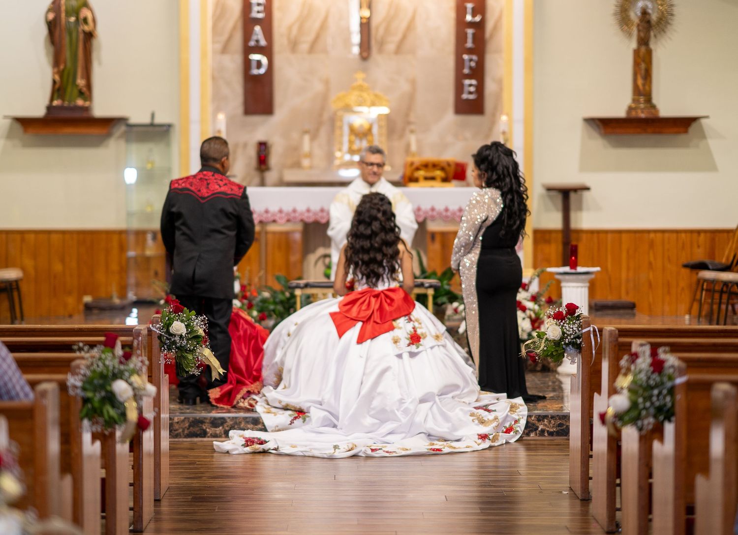 A traditional Catholic wedding ceremony in progress at a church altar decorated with red and white floral arrangements.