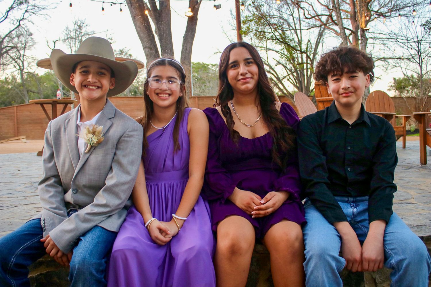 Family sits together on outdoor bench wearing coordinated purple and casual attire.