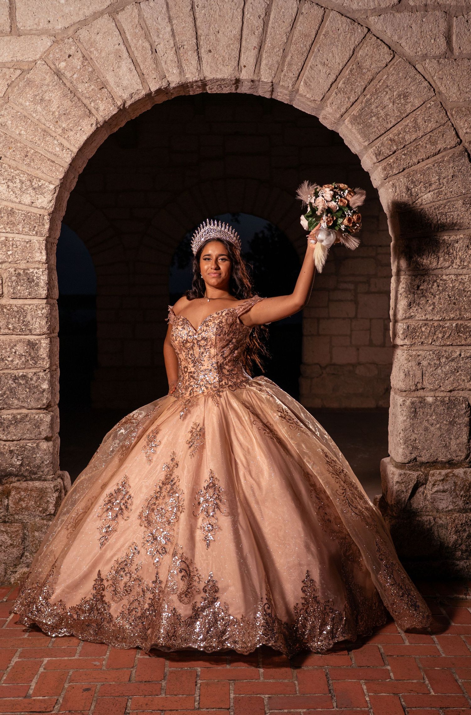 A ornate pink ballgown with sequins photographed under stone archways in dramatic lighting.
