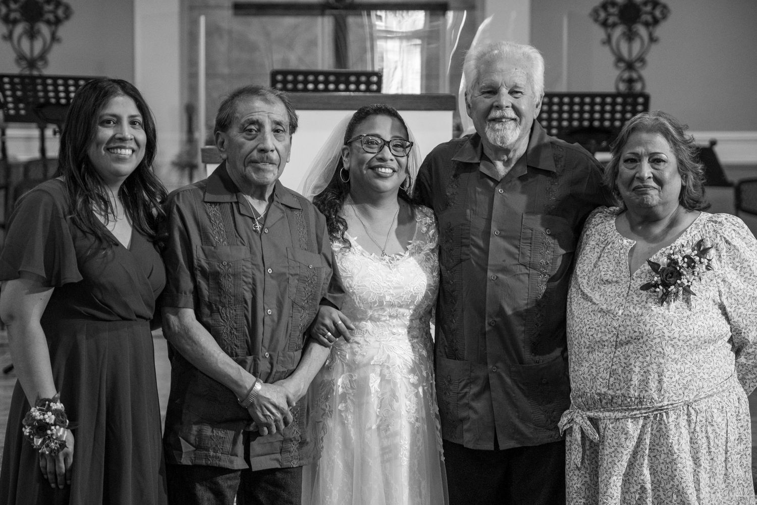 Black and white photo of a bride in white dress posing with four smiling family members at a wedding celebration.