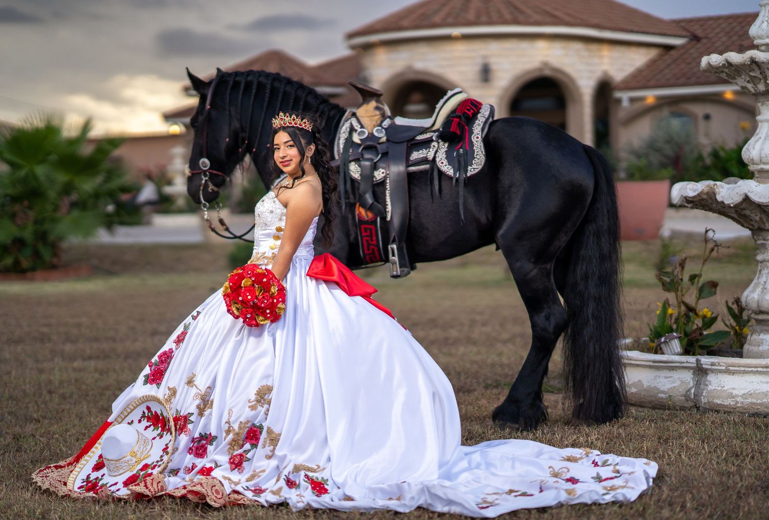 A white dress with red floral details spreads across the ground near a black horse.