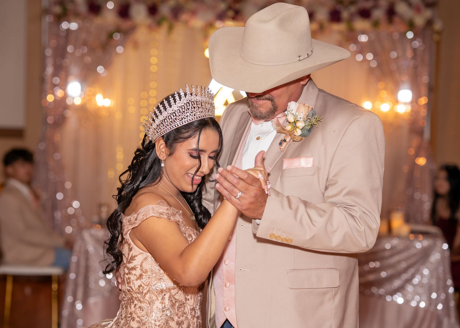 A Quinceañera in a rose gold gown and crown shares a tender dance moment with her father in a tan cowboy suit.