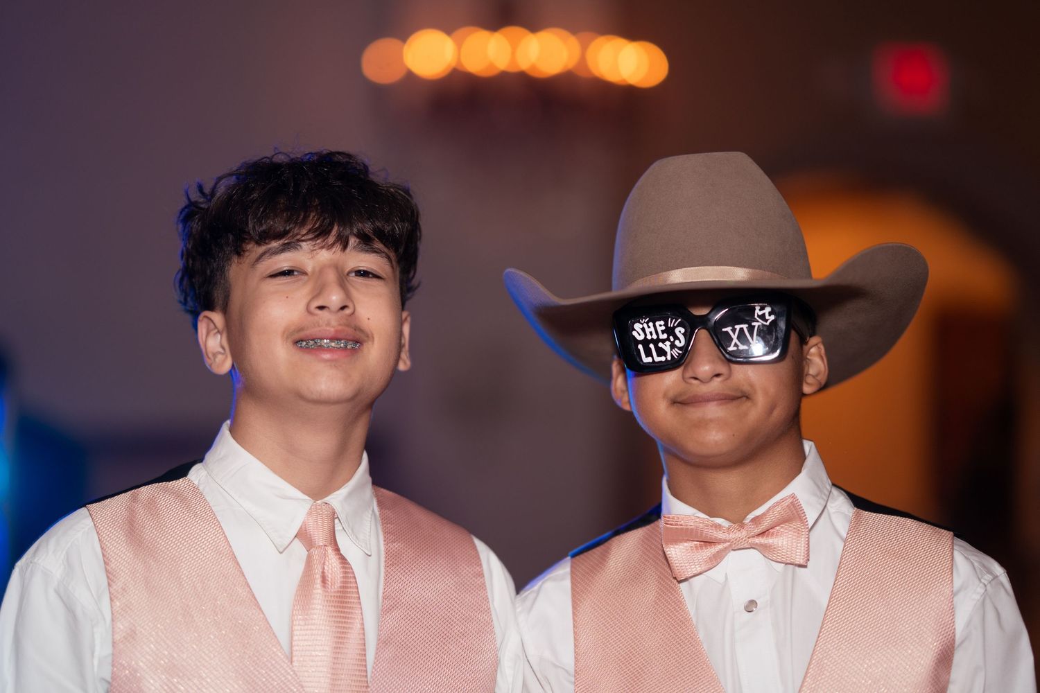 Two young boys in pink formal wear and cowboy hats smiling at a quinceañera party.