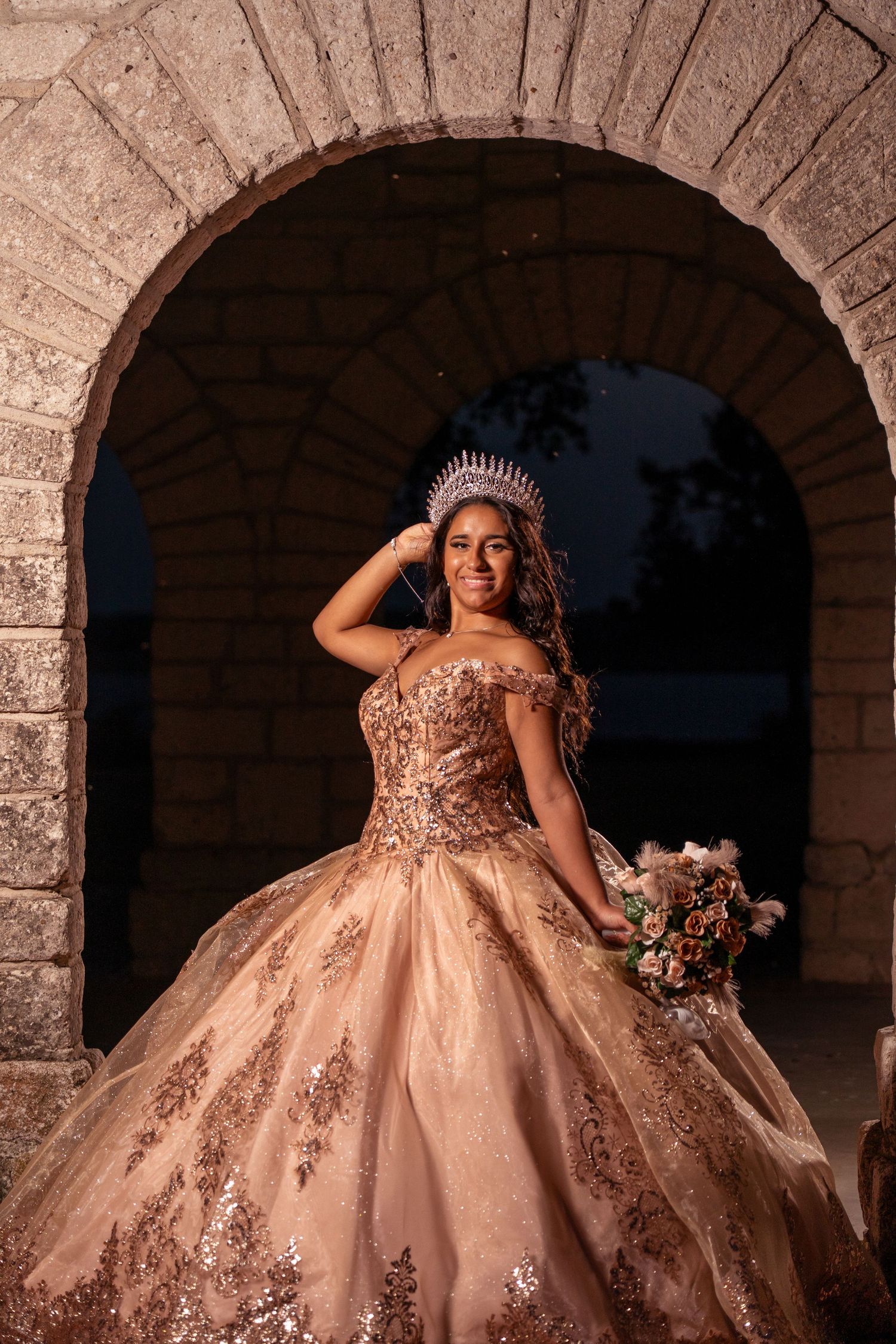 A formal portrait shows an ornate champagne-colored ball gown framed by a classic stone archway.