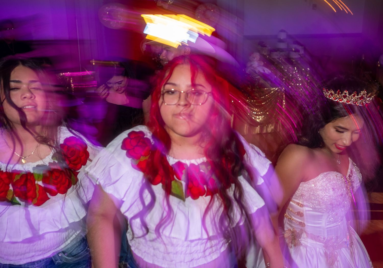 People in white dresses dance and celebrate at a party with purple lighting and festive atmosphere.