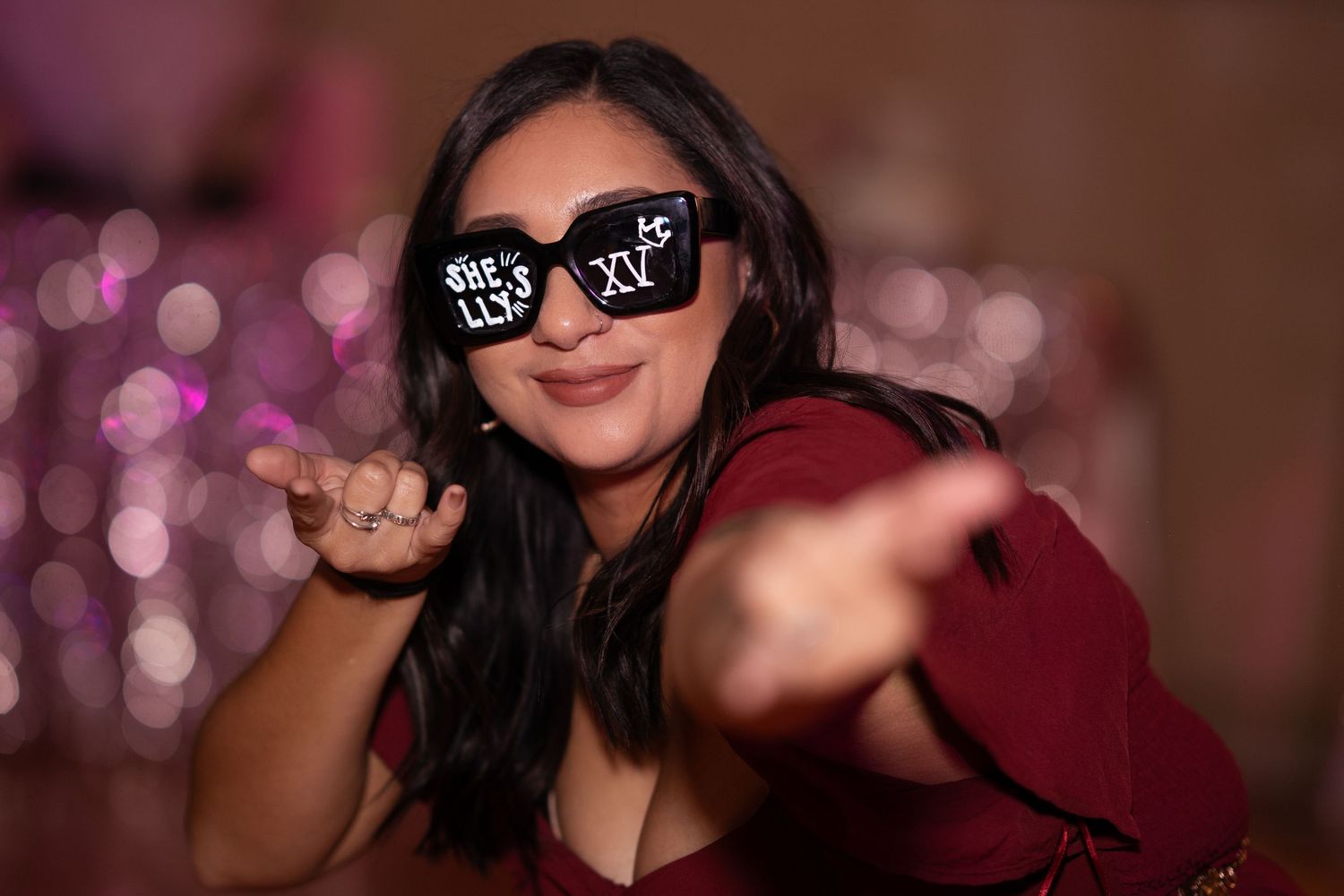 Woman wearing novelty sunglasses blows a kiss at a festive quinceañera celebration.