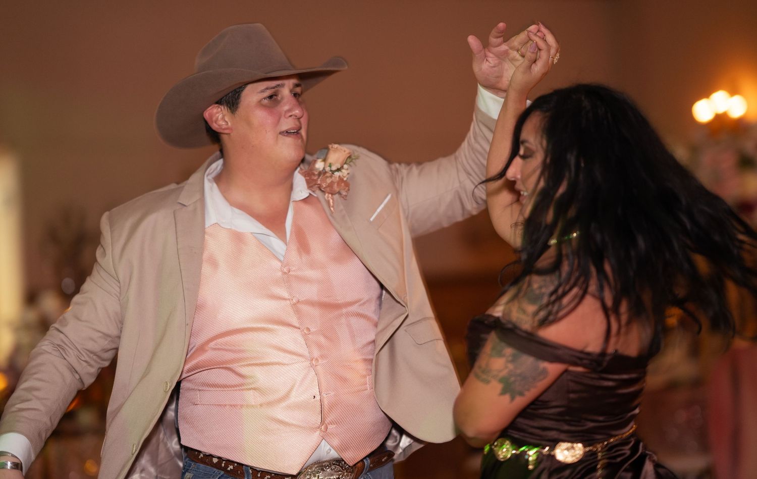 Man in tan cowboy hat and suit dancing energetically with woman at a quinceañera reception.