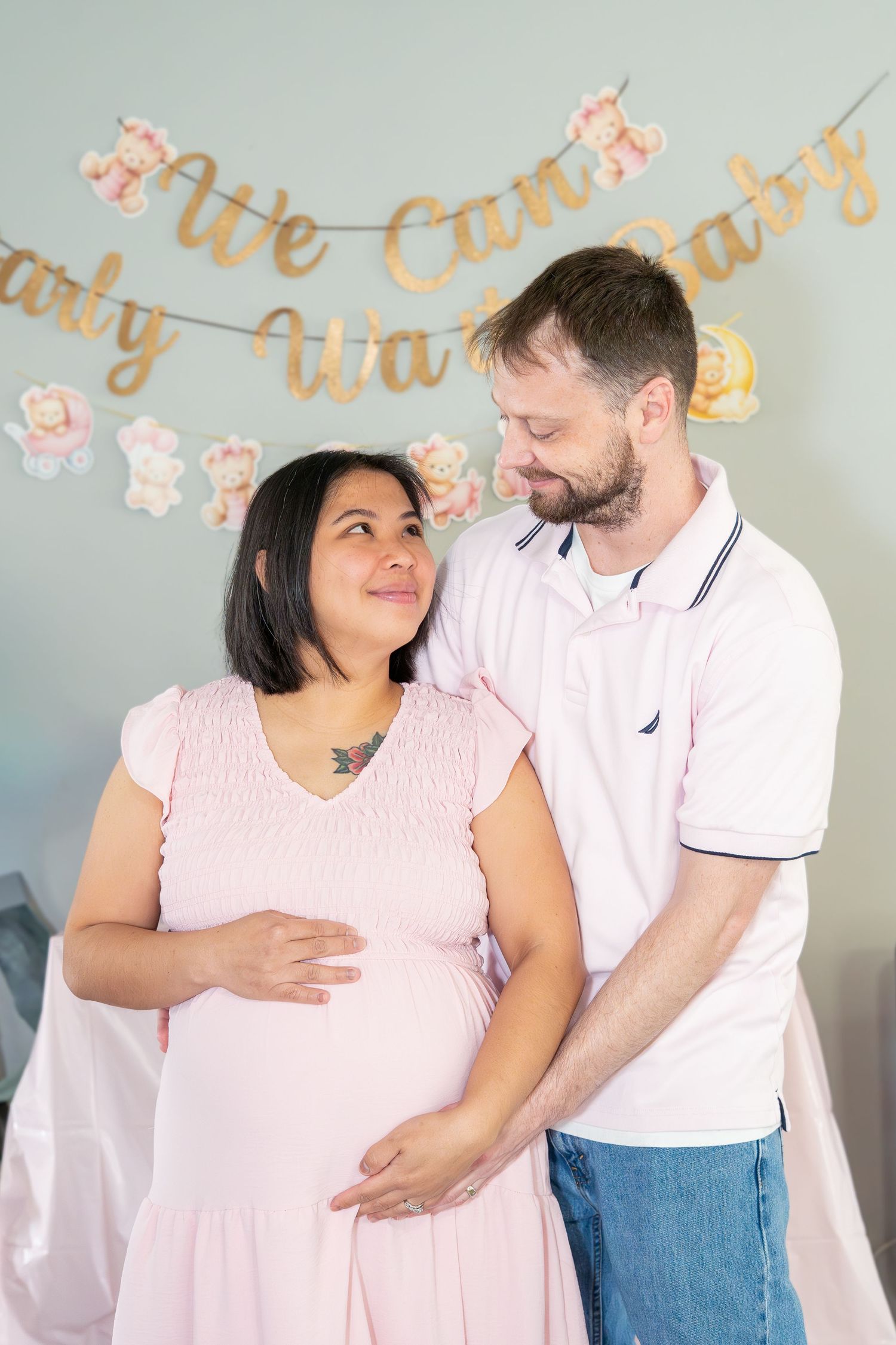 Pregnant couple tenderly gazing at each other at a baby shower with gold banners.