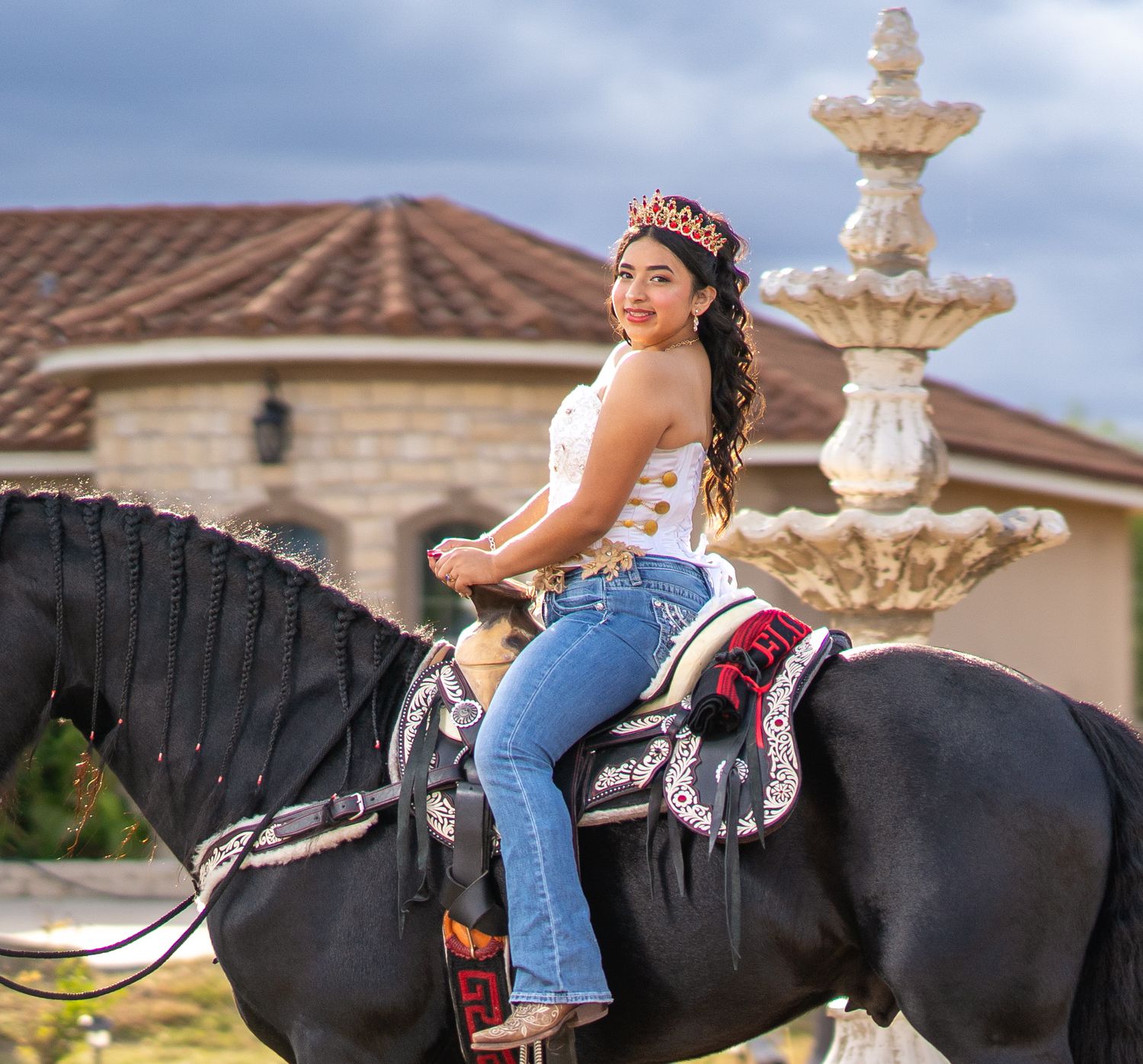 A person in blue jeans rides a dark horse in front of a residential building at sunset.