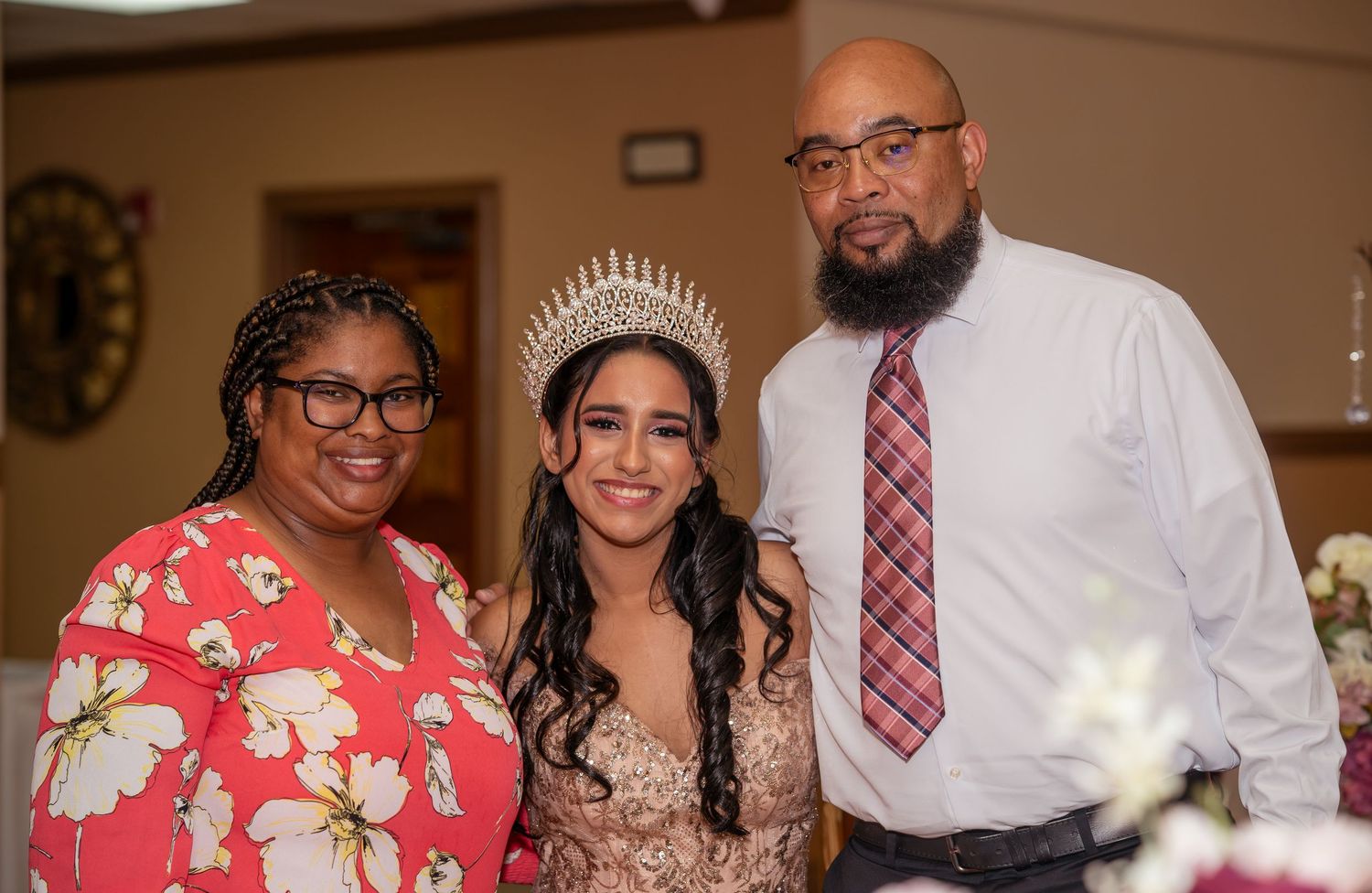 Three people posing together at a quinceañera, with young woman wearing tiara and gown.