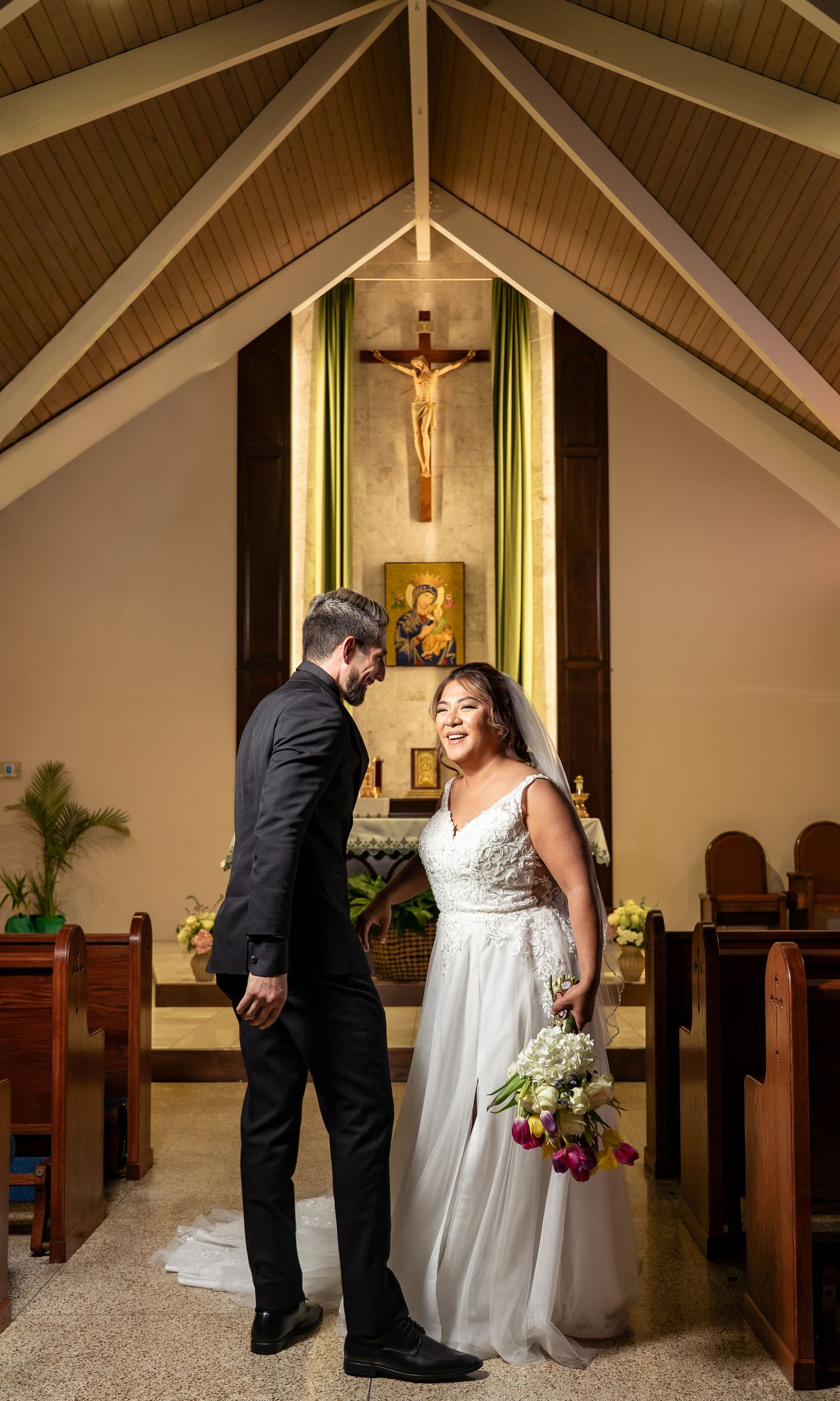 A couple shares an intimate moment during their wedding ceremony in a church with wooden beams and religious decor.