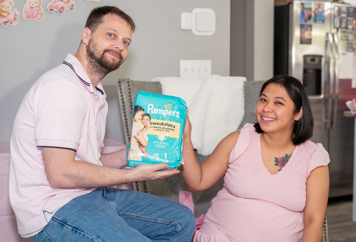 Pregnant woman and man holding a pack of Pampers diapers together in a nursery room.