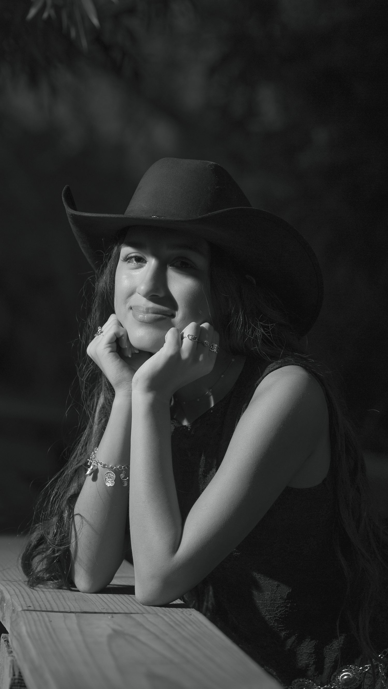 Black and white portrait of a smiling young woman in a cowboy hat, resting her chin on her hands.