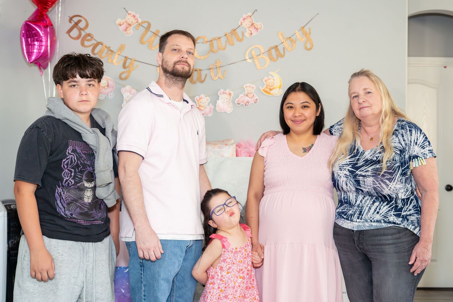 Family posing together at a baby shower with pink decorations and a banner in the background.