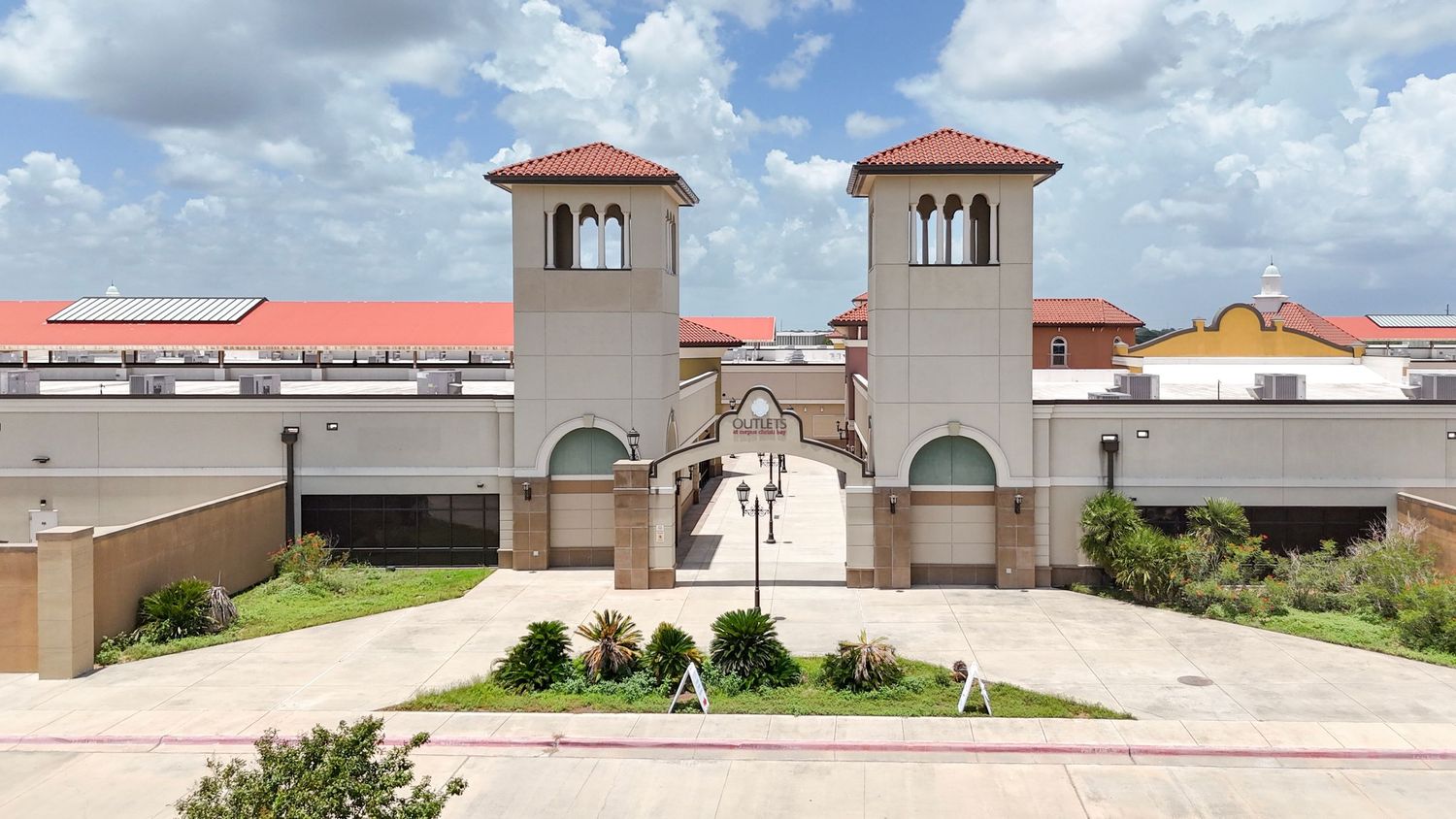 Panoramic view of a commercial plaza with red tile roofs and arched windows under partly cloudy skies.
