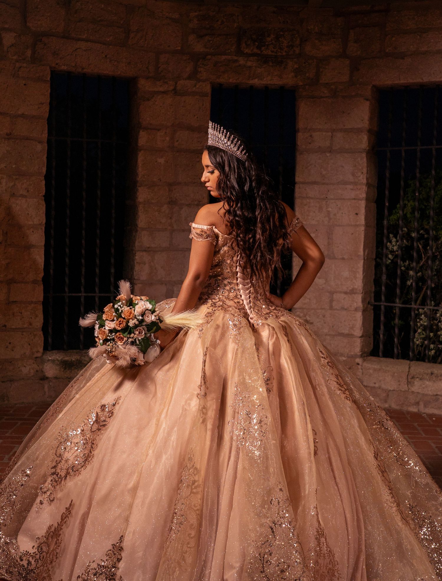 Rose gold princess gown with detailed embroidery and floral bouquet photographed in vintage brick setting.
