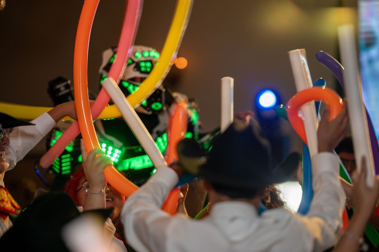 People wave colorful glowing lightsabers in a dark room during an energetic event celebration.