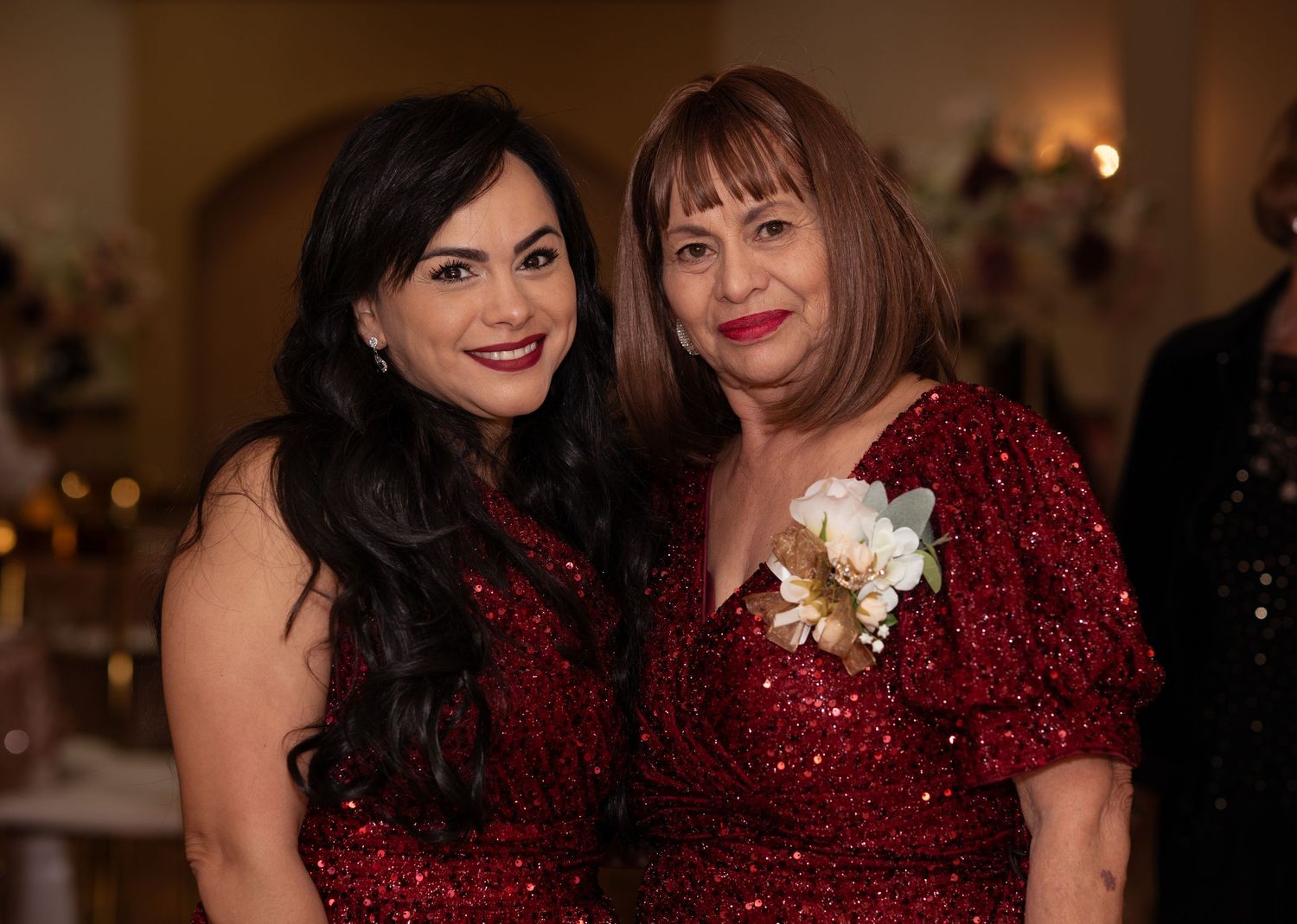 Two women in matching red sequin dresses pose together smiling at a formal event.