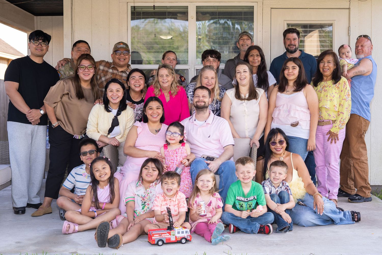 Large diverse family group photo with adults and children posing together outdoors on a home porch.