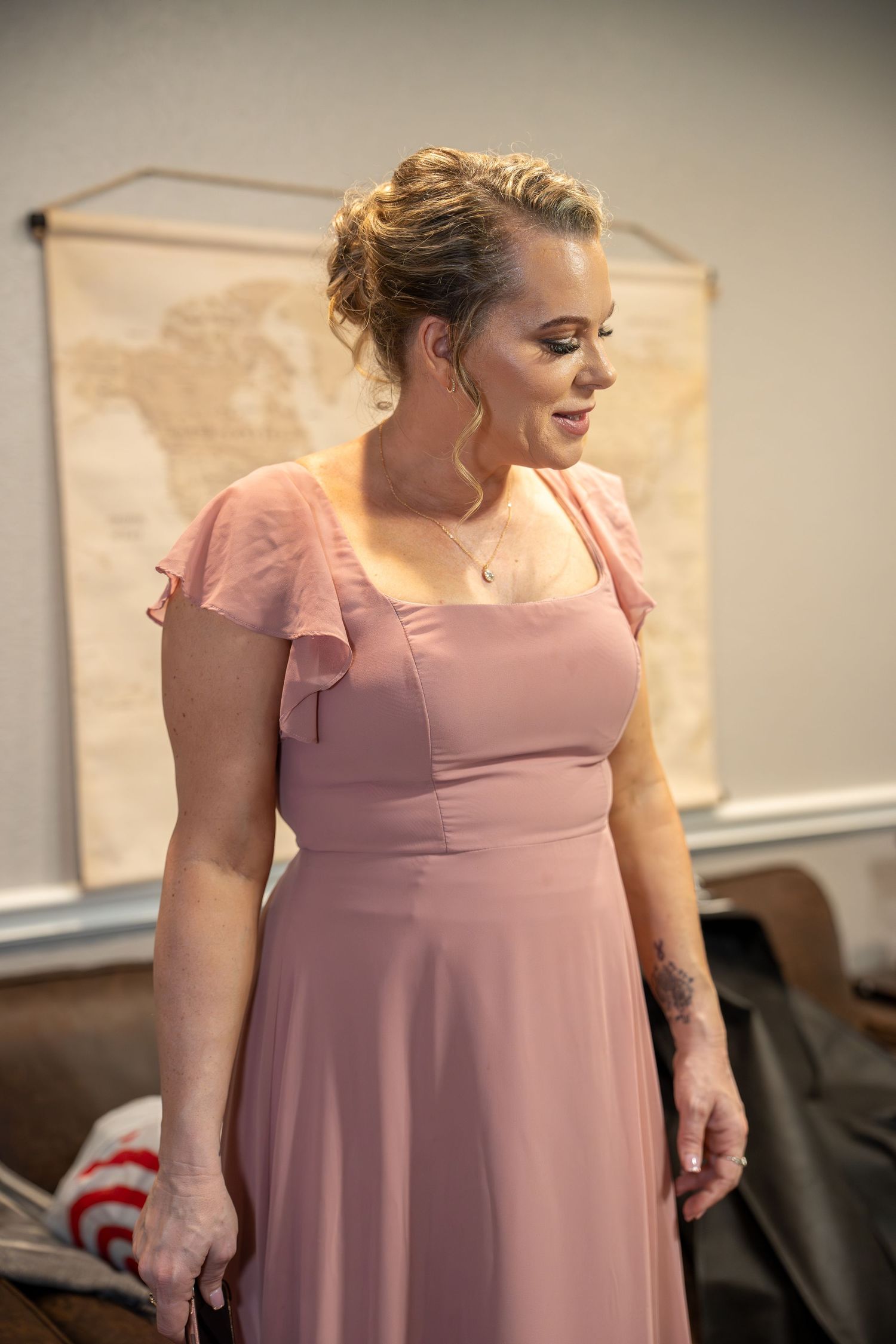 Woman in pink maxi dress with flutter sleeves stands elegantly in a room with a vintage world map backdrop.