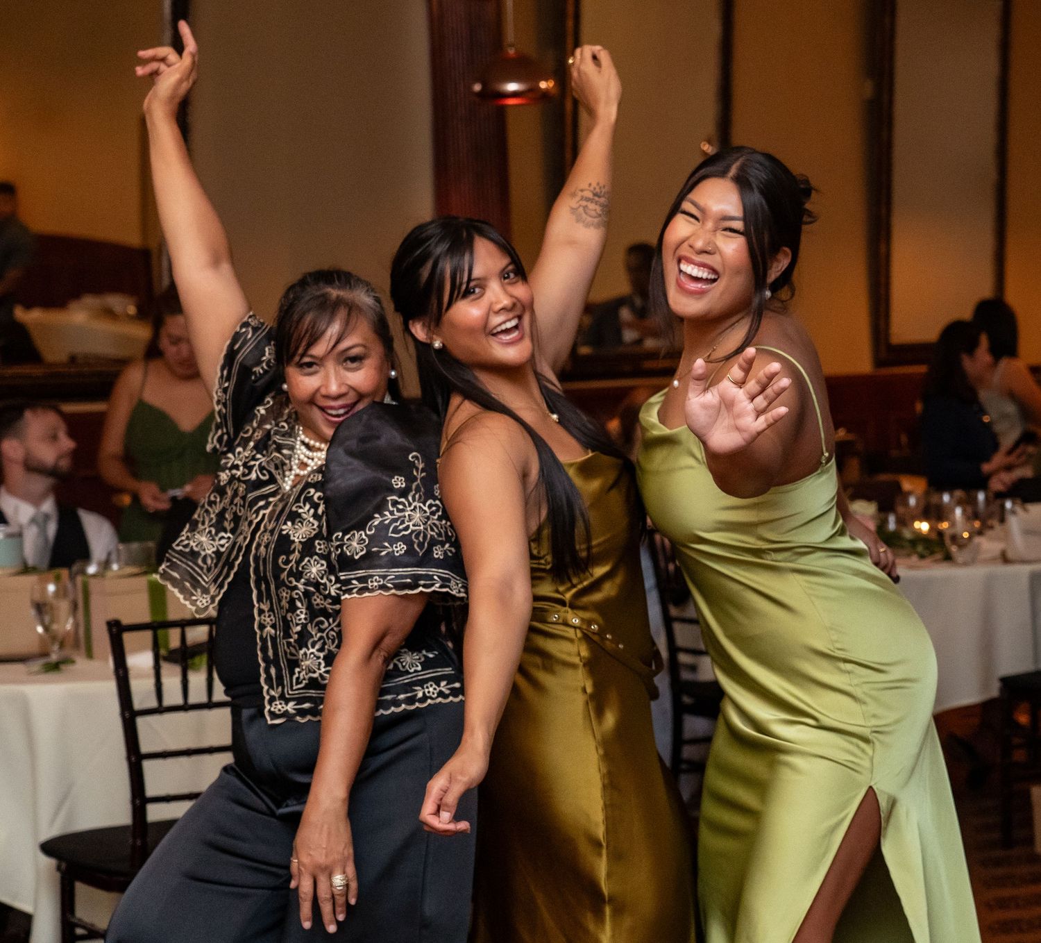 Wedding guests in black and chartreuse dresses dance and laugh together at a reception celebration.