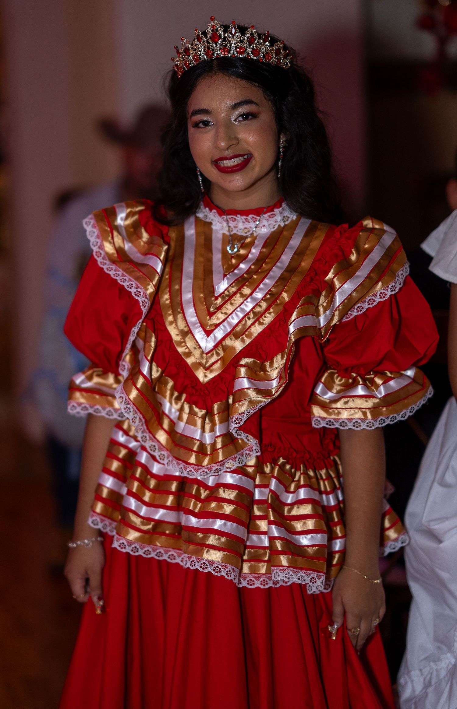 Dancers wearing traditional red and white ruffled dresses with lace trim perform in a cultural celebration.