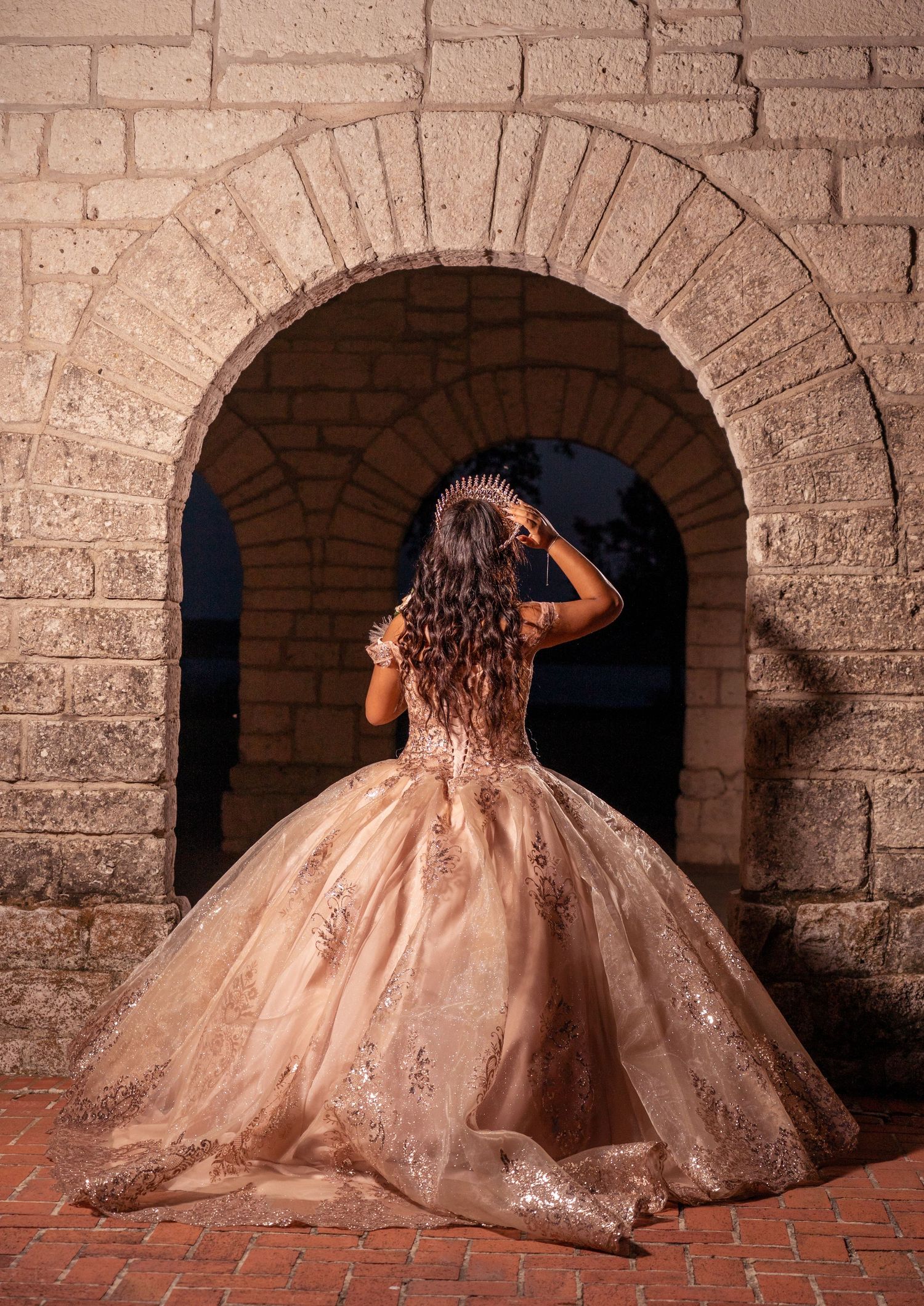 Beautiful ball gown with sparkly details twirling under stone archway at dusk.