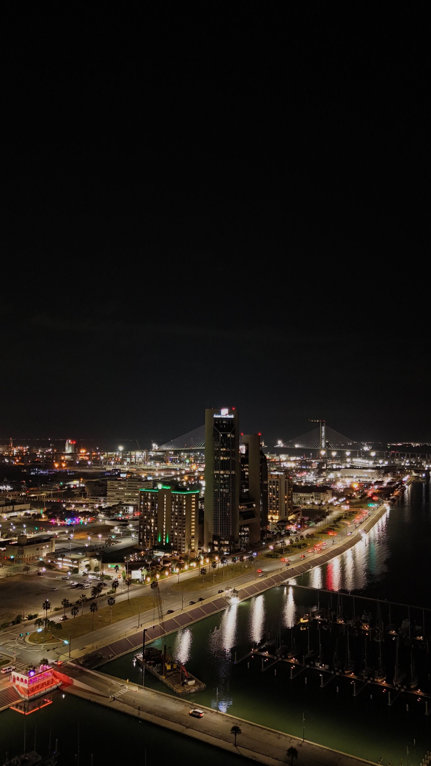 Nighttime cityscape of waterfront buildings in Long Beach with illuminated skyscrapers reflecting on marina waters.