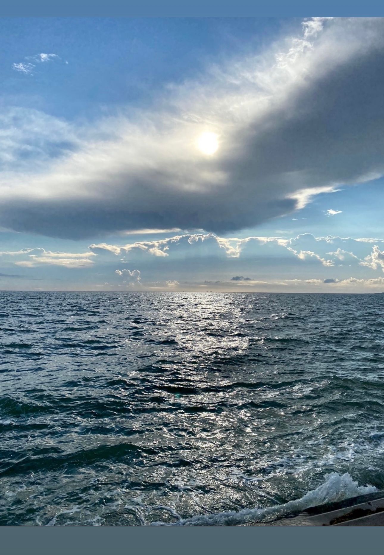 Sunlight breaks through dramatic clouds over choppy ocean waves creating a shimmering seascape.