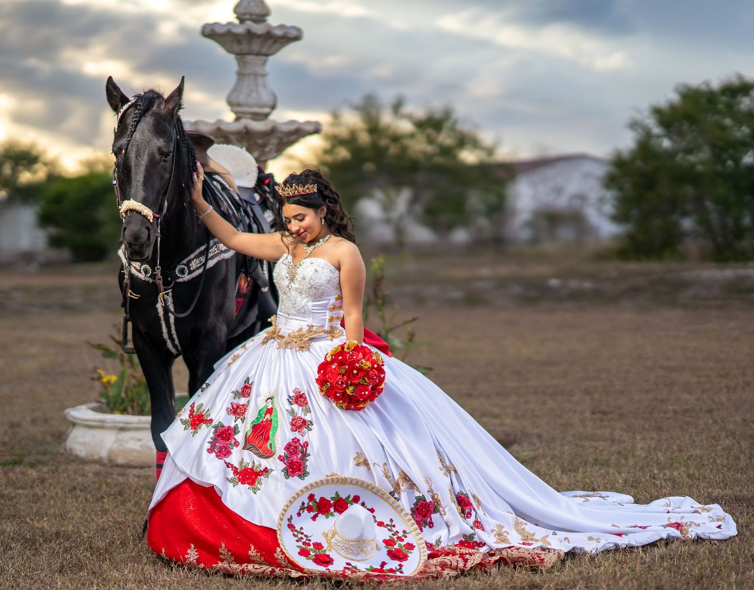 A stunning white and red dress with floral details spreads across the ground next to a black horse.