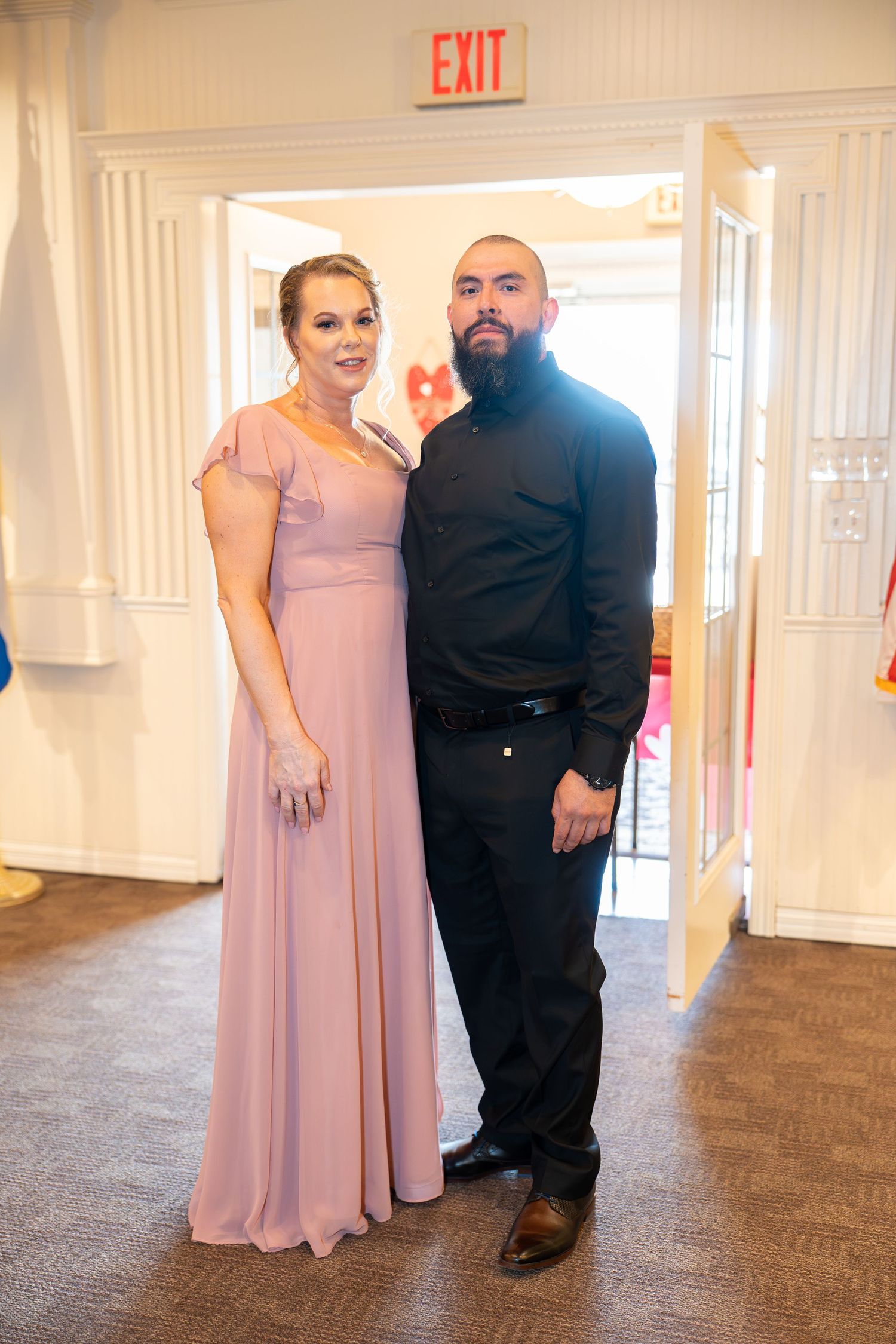 Couple posing at wedding reception, woman in blush pink gown and man in black shirt and pants.