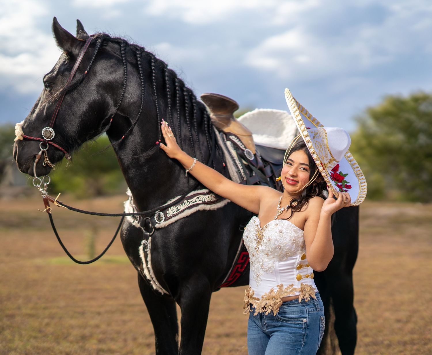A stunning quinceañera photo shoot featuring a beautiful white and red dress alongside a majestic black horse in a field.