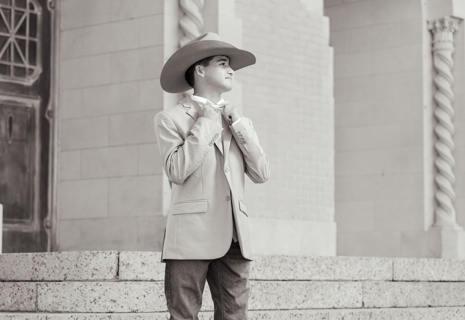 A person in a cowboy hat and suit jacket stands on stone steps outside a building in a vintage black and white photograph.
