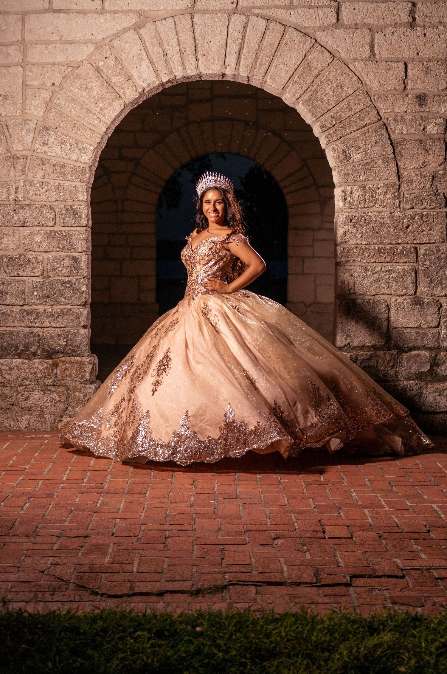A princess-style gown with detailed embroidery shimmers beneath a rustic stone arch.